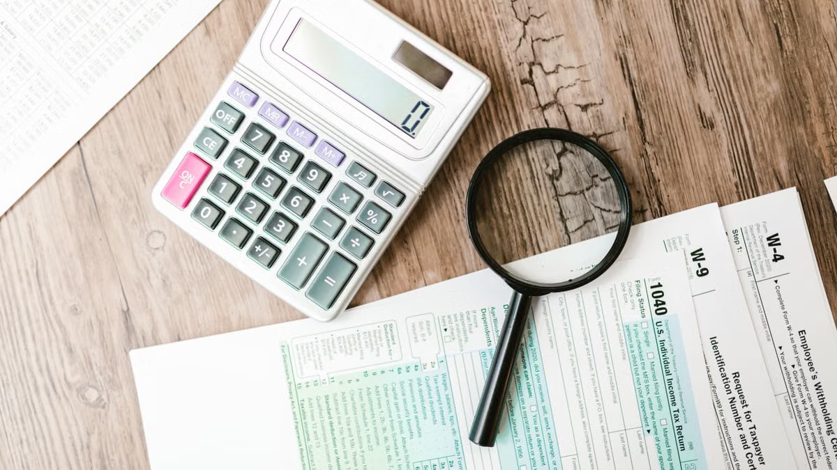 Tax forms laid out with a calculator and magnifying glass on a wooden surface, perfect for finance themes.
